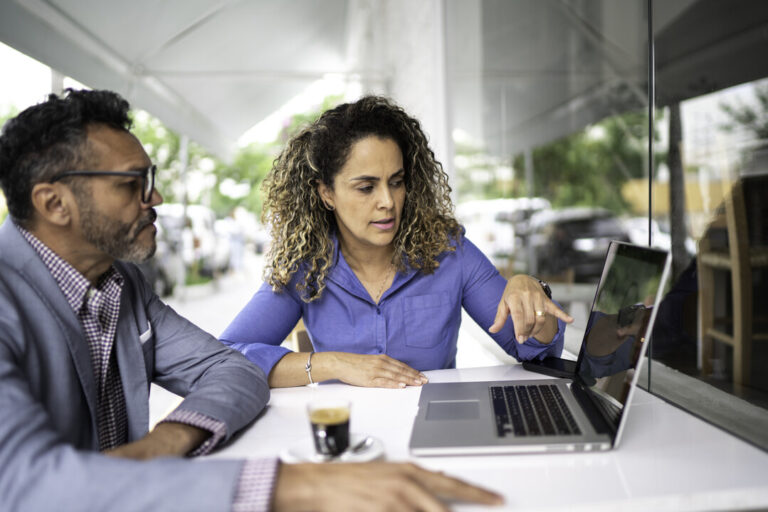 a man and woman sitting at a table looking at a laptop