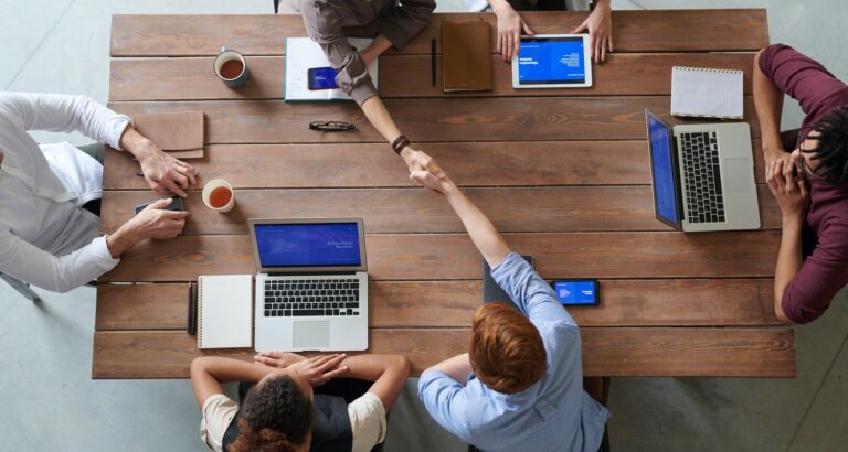 people shaking hands at a table with laptops and tablet computers